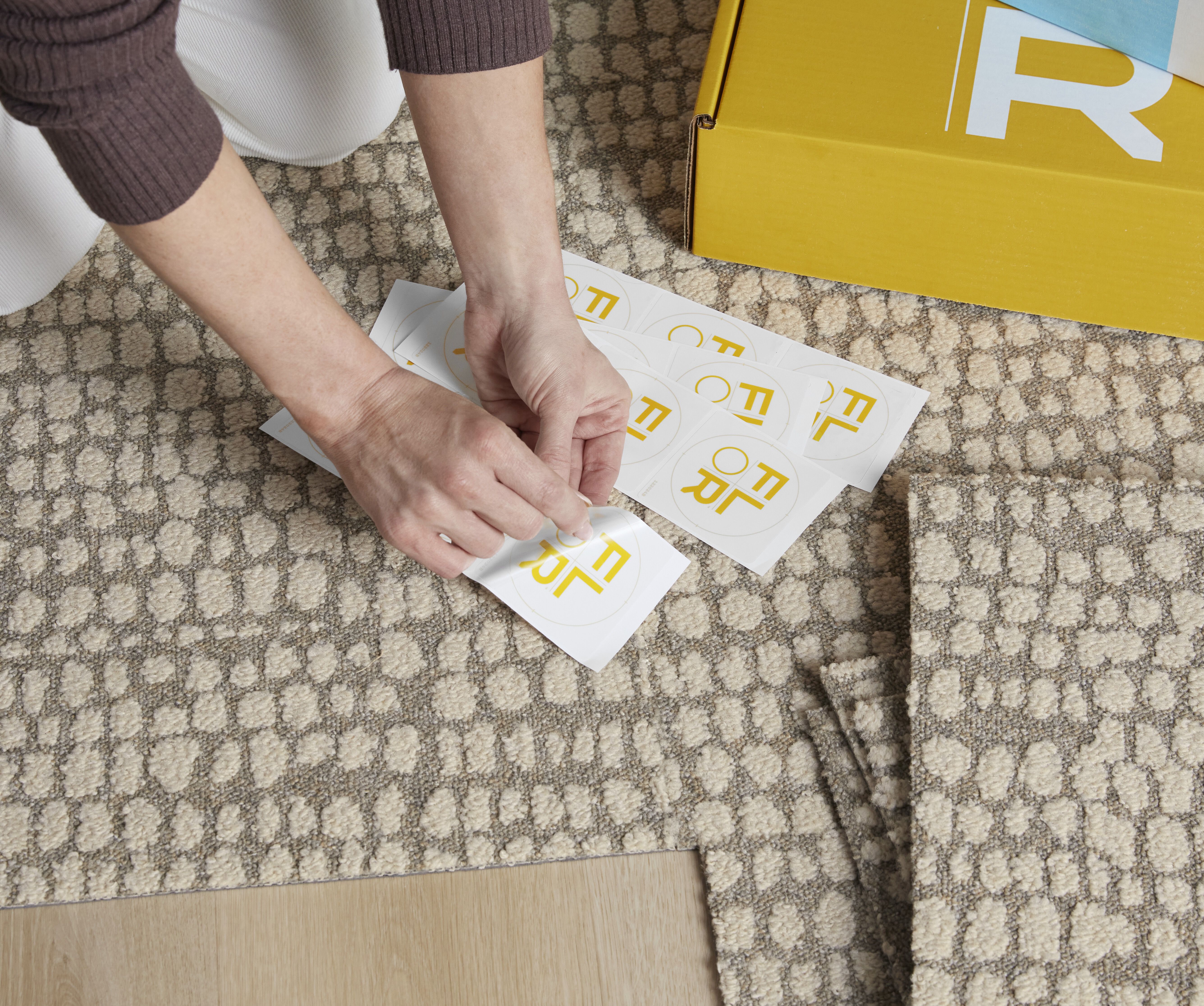 Hands of a person using a FLORdot to assemble a FLOR area rug from carpet tiles.